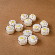 Tealight candles with white daisy flower tops on brown surface
